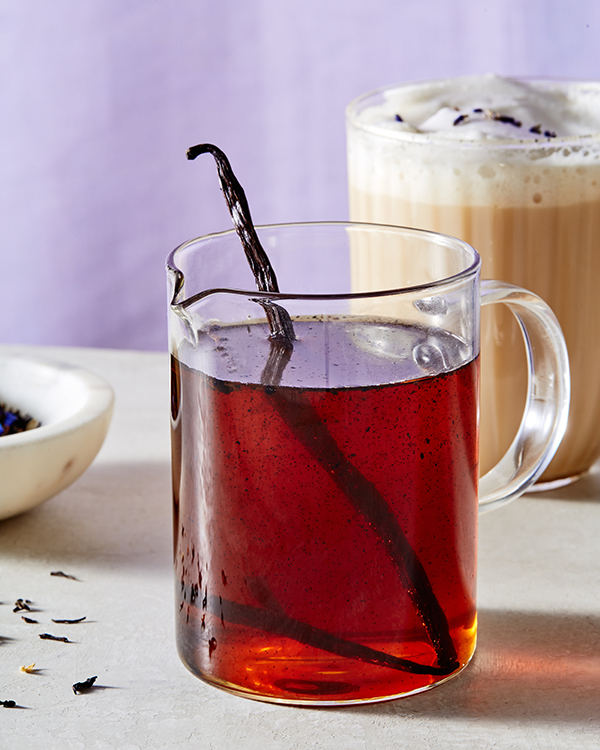 Une carafe en verre de sirop simple à la vanille avec un pod de gousse de vanille, montrée avec un verre à latte London Fog et un plat de thé Earl Grey en vrac.