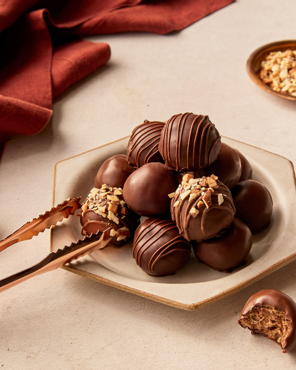  Un tas de bouchées de pâte à biscuits trempées dans le chocolat sur une assiette hexagonale, servies avec des petites pinces.