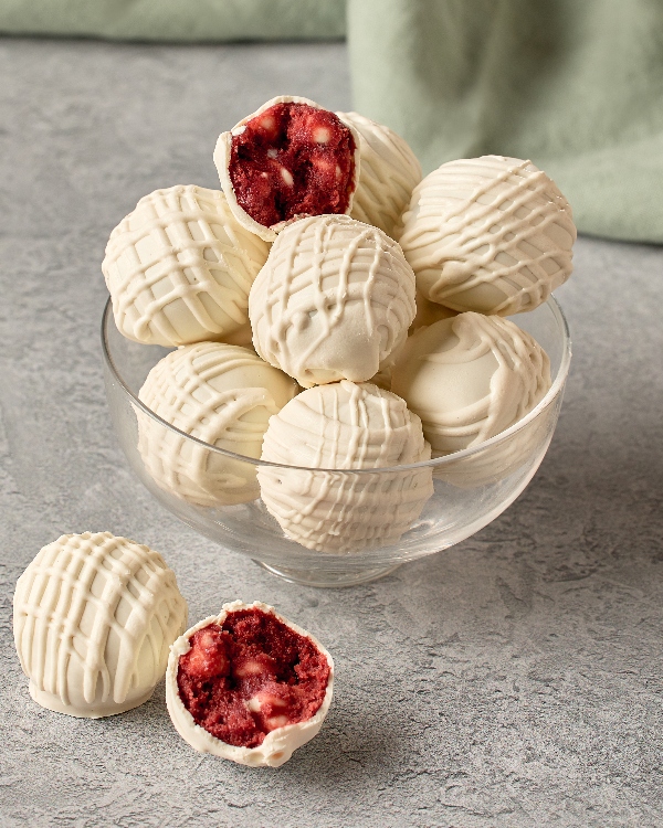 Un verre de truffes de pâte à biscuits velours rouge trempées dans le chocolat blanc avec un filet (ou un glaçage en zig-zag). L'une d'elles est montrée coupée en deux, avec le centre rouge visible.