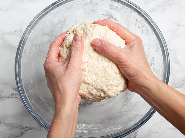 eux mains qui tiennent une boule de pâte brisée au-dessus d’un bol en verre