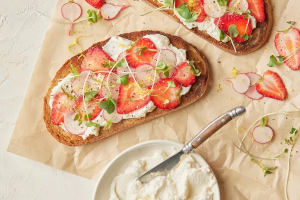 Deux tranches de pain grillé garnies de ricotta fouettée à la cassonade, de fraises et de radis tranchés, ainsi que de micro-pousses.