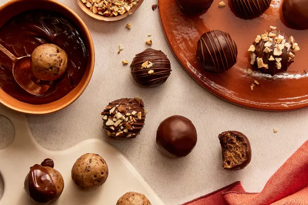 Des bouchées de pâte à biscuits trempées dans le chocolat à différents stades de préparation, certaines saupoudrées de noix, une avec une bouchée en moins.