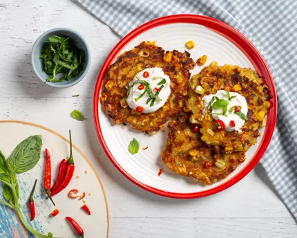 Croquettes de maïs et chili sucré sur assiette rouge et blanche avec crème sûre et herbes