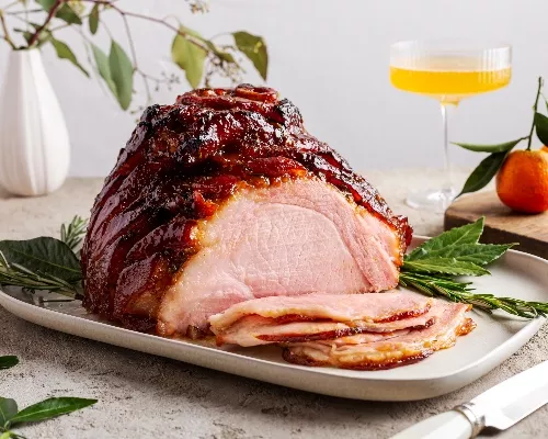Jambon glacé rôti sur un plateau et garni d'herbes avec plusieurs tranches coupées