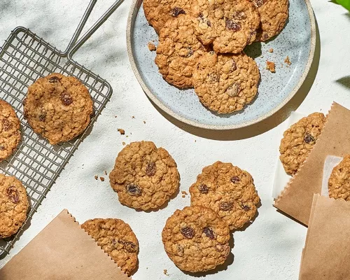 Biscuit moelleux avoine et raisins sur une assiette, une grille de refroidissement, une table et dans des enveloppes de papier