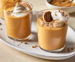 Trois verres de pudding au caramel écossais sur un petit plateau ovale, chacun garni de crème fouettée, de morceaux de toffee et de biscuits. 