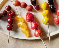 Un plateau de fruits et de baies en brochettes enrobés de sirop de sucre clair, ou tanghulu, incluant des segments de mandarine, des cerises, des raisins, des groseilles à maquereau, des fraises, des kumquats et des mûres.