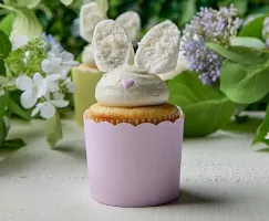  Cupcakes au citron décoratifs sur le thème de Pâques avec un glaçage à la crème au beurre et des oreilles de lapin en guimauve trempées dans la noix de coco, présentés dans des caissettes à cupcakes pastel, parfaits pour un dessert de printemps festif.