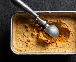 Crème glacée aux carottes dans un récipient en métal avec une cuillère à crème glacée
