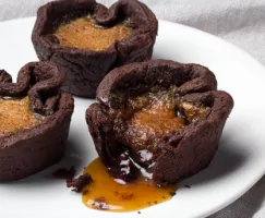 Tartelettes au beurre chocolatées disposées sur une assiette, dont une avec sa garniture qui coule