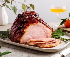 Jambon glacé rôti sur un plateau et garni d'herbes avec plusieurs tranches coupées