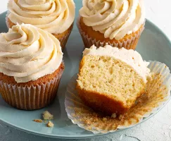 Sur une assiette, quatre cupcakes à la vanille avec glaçage, dont un coupé en deux