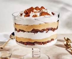Un gâteau au fromage au potiron de taille familiale dans un grand bol en verre à pied avec des biscuits émiettés sur le dessus.