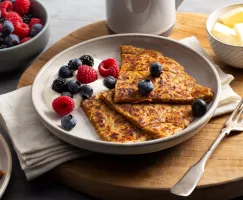 Farl à la patate douce sur une assiette avec de la crème et des petits fruits, servi avec du beurre et un bol de petits fruits