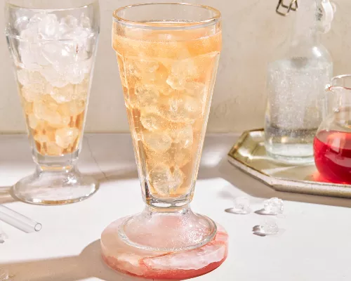 Deux verres de julep à la menthe sans alcool avec de la glace pilée et garnis de menthe, servis sur un plateau blanc et présentés avec un bol de feuilles de menthe, une moitié de lime, une carafe de julep préparé et une carafe de sirop simple à la menthe.