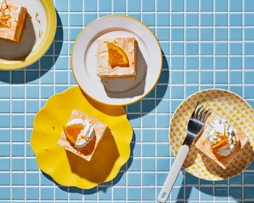 Quatre morceaux de gâteau glacé à la vanille et à l'orange dans des assiettes sur un comptoir carrelé bleu.